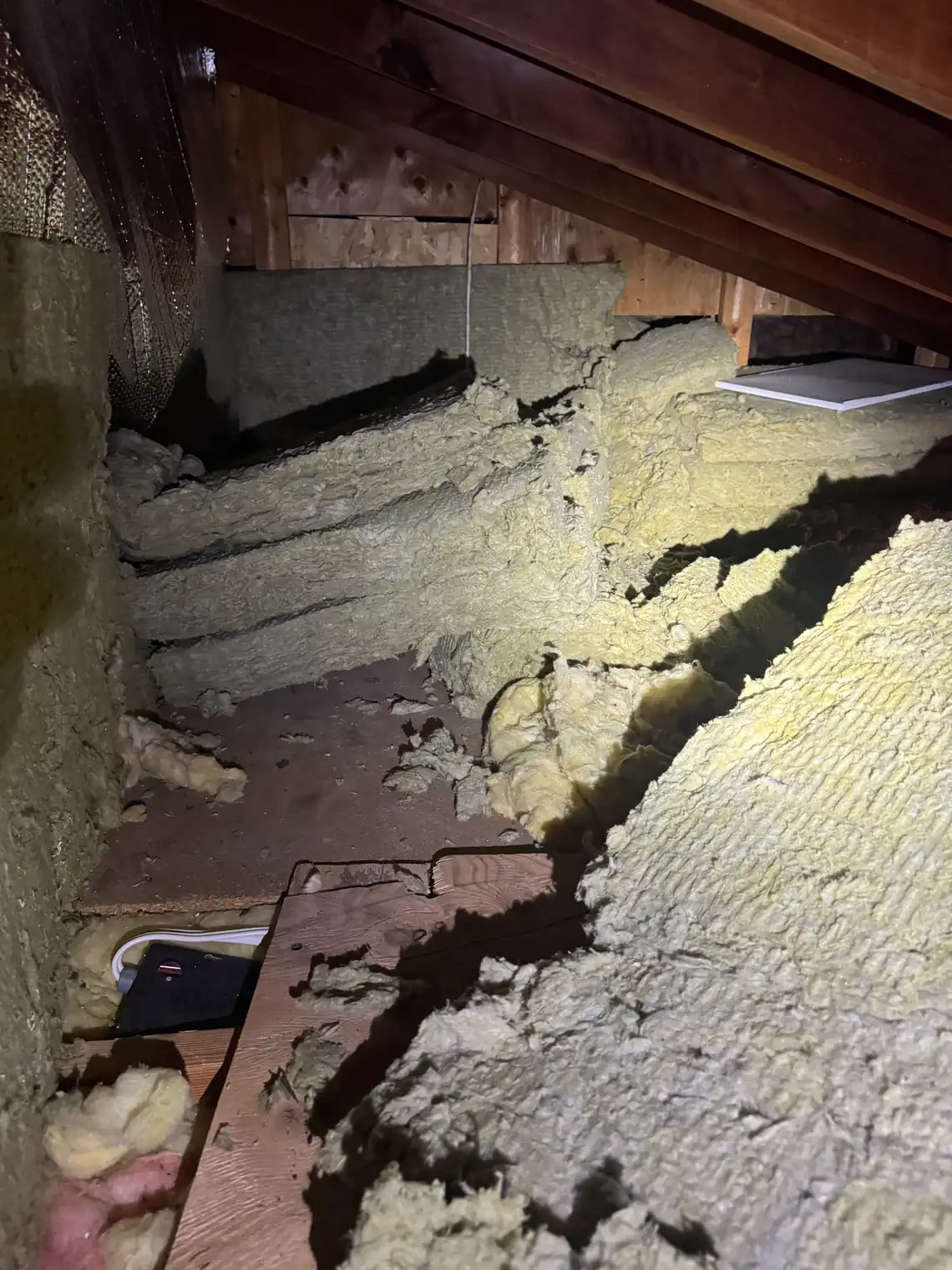 Fibreglass batt in a BC attic laid short of the edges, leaving bare boards and gaps along the joists