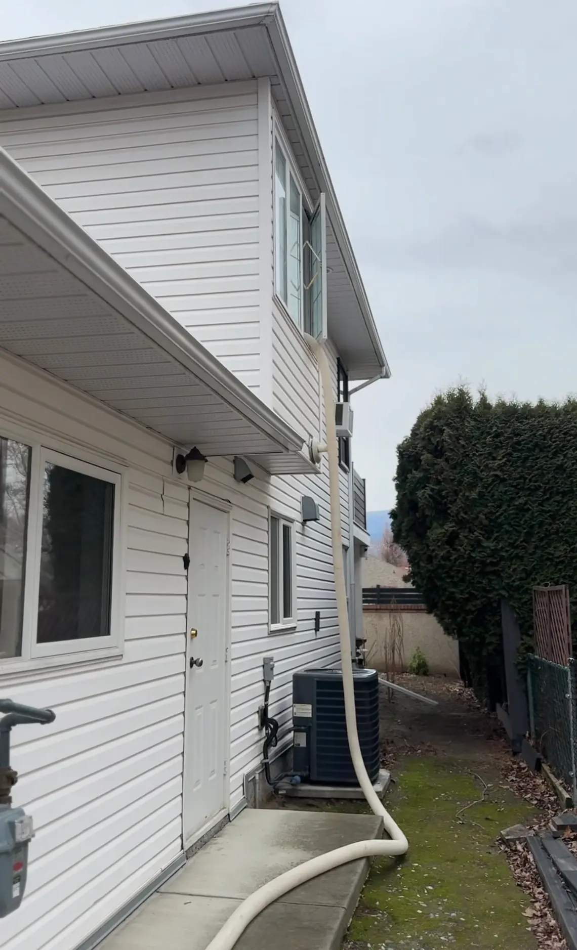 A blow-in hose running up the outside of a BC house and in through an upstairs window on a grey winter day