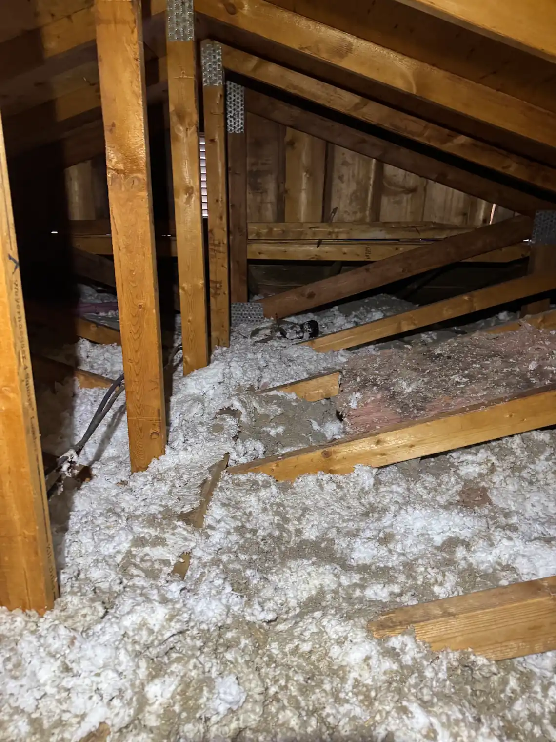 A BC attic with thin patchy fibreglass insulation between the joists and bare wood showing through in places