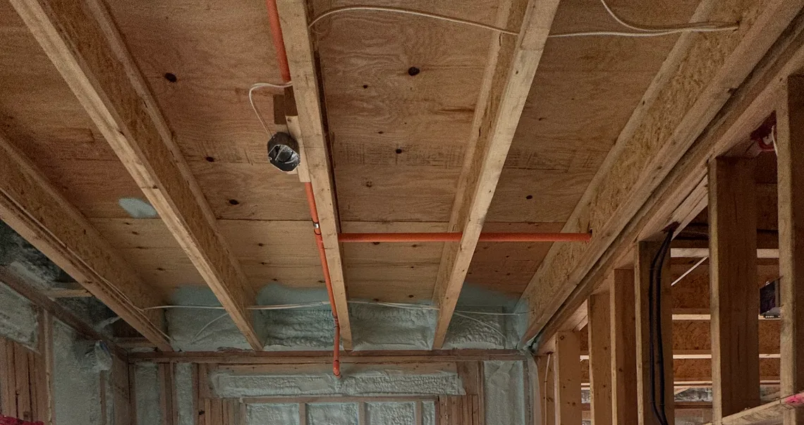 Closed-cell spray foam packed into the floor joist ends above a framed wall on a BC job