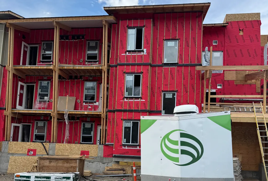 A three-storey wood-frame rental building in Kamloops BC wrapped in red weather membrane, windows in, siding not yet started